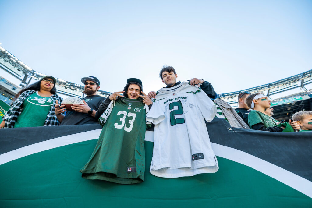 Two fans in the Jets stadium, holding up jerseys.