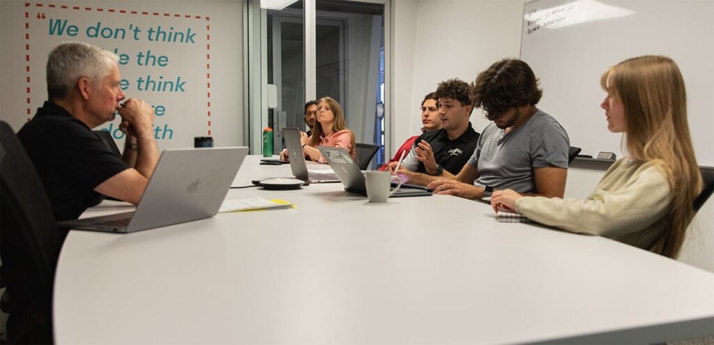 A team of students speaks in a conference room with a Cal Poly Alumnus