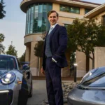 Alumni poses with two Porsches outside business building