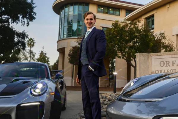 Alumni poses with two Porsches outside business building