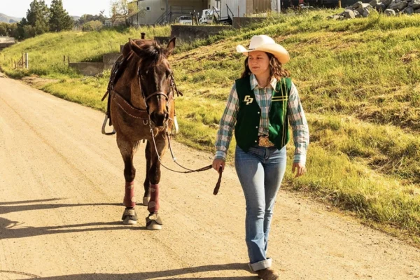 A rodeo member walks her horse down a trail